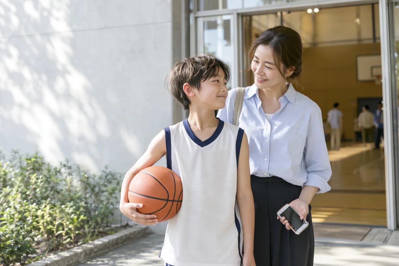 バスケットボールを抱えた子どもと、スマートフォンを持つ保護者